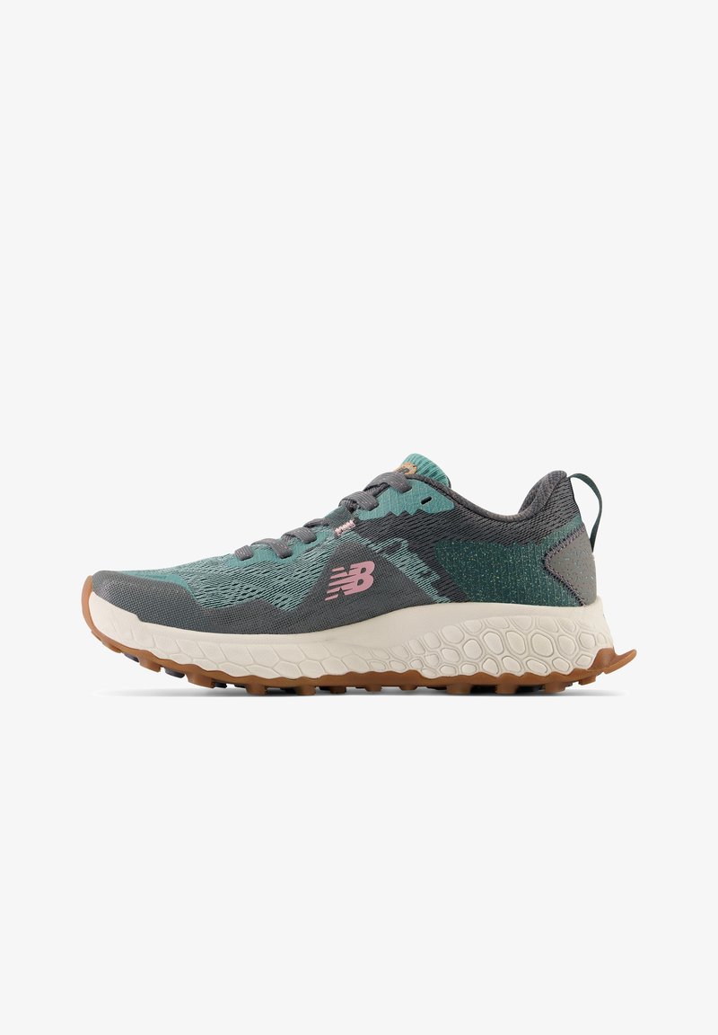 Zapatilla de running New Balance en gris y tonalidades verde azulado con logo rosa, entresuela blanca texturizada y suela marrón rugosa, vista lateral.