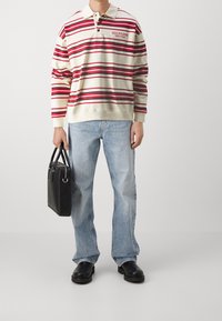 Gestreifter Sweatshirt in Creme, Rot und Marineblau; mit Kragen und Knopfverschluss. Hellblaue Jeans, schwarze Tasche und schwarze Clogs runden das Outfit ab.
