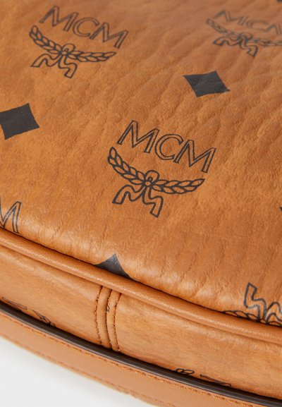 Surface en cuir tan avec des logos MCM noirs et des formes de diamant sur un coin de sac texturé avec des bords cousus.