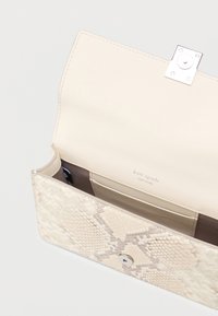 Τσαντάκι φάκελος σε μπεζ χρώμα με υφή φιδίσιας επιδερμίδας και μαγνητικό κλείσιμο, ανοιχτό για να φαίνονται οι εσωτερικές θήκες για κάρτες και το λογότυπο "kate spade new york".