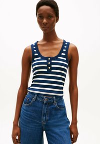 Top de tirantes a rayas en azul marino y blanco con escote redondeado y tres botones dorados. Combinado con unos jeans de talle alto en azul. Tejido suave y ajustado.