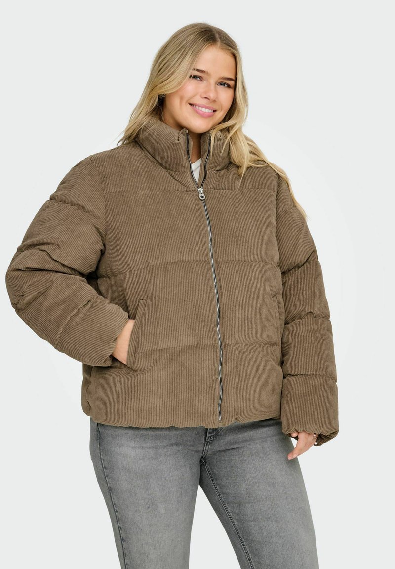 Smeđa pulover jakna od šuškavog materijala s visokim ovratnikom, patentnim zatvaračem i bočnim džepovima. Ima prošivenu teksturu. Nošena je s sivim trapericama.