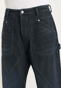 Donkerdenim jeans met een hoge taille, meerdere gestructureerde zakken en unieke hoekige ontwerpen aan de voorkant. Zilveren hardware accenten aanwezig.