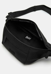 Curea de mână neagră din material textil cu o textură netedă, închidere cu fermoar și etichetă interioară. Are o curea ajustabilă pentru o purtare sigură.