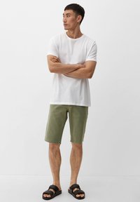 Biała bawełniana koszulka z okrągłym dekoltem, zielone szorty dżinsowe i czarne sandały. Prosty design z luźnym krojem i szortami do kolan.