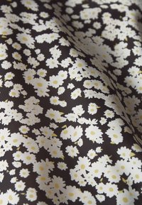 Tkanina s tmavým pozadím a opakujícími se vzory malých bílých sedmikrásek se žlutými středy, vytvářející texturovaný květinový design.