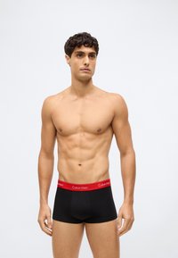 Černé bavlněné boxerky s červeným pasem, s logem "Calvin Klein". Hladká textura, těsný střih a střední délka.