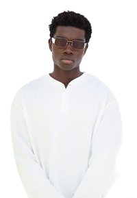 Camicia bianca a maniche lunghe con scollatura henley. Gli accessori includono occhiali da sole rettangolari con lenti scure e rifiniture argentate.