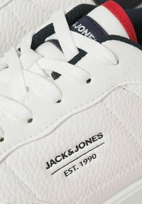 Gros plan sur une basket blanche Jack & Jones en cuir texturé, lacets blancs et marquage "Jack & Jones Est. 1990" sur le côté.