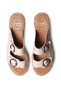 Sandali color beige chiaro con due cinturini decorativi dotati di fibbie nere circolari. Parte superiore texturizzata con una soletta in pelle liscia e suola in juta intrecciata.