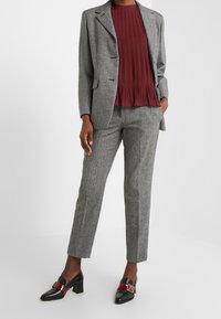 Grå tweedblazer med klassisk slag, kombinerad med en vinröd veckad topp och matchande skräddarsydda byxor, kompletterad med svarta skor med röda accenter.