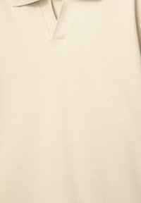 Beige polo shirt med V-halsdesign, der har et blødt, tekstureret stof og ribbet krave. Simpel, minimalistisk uden yderligere mønstre.
