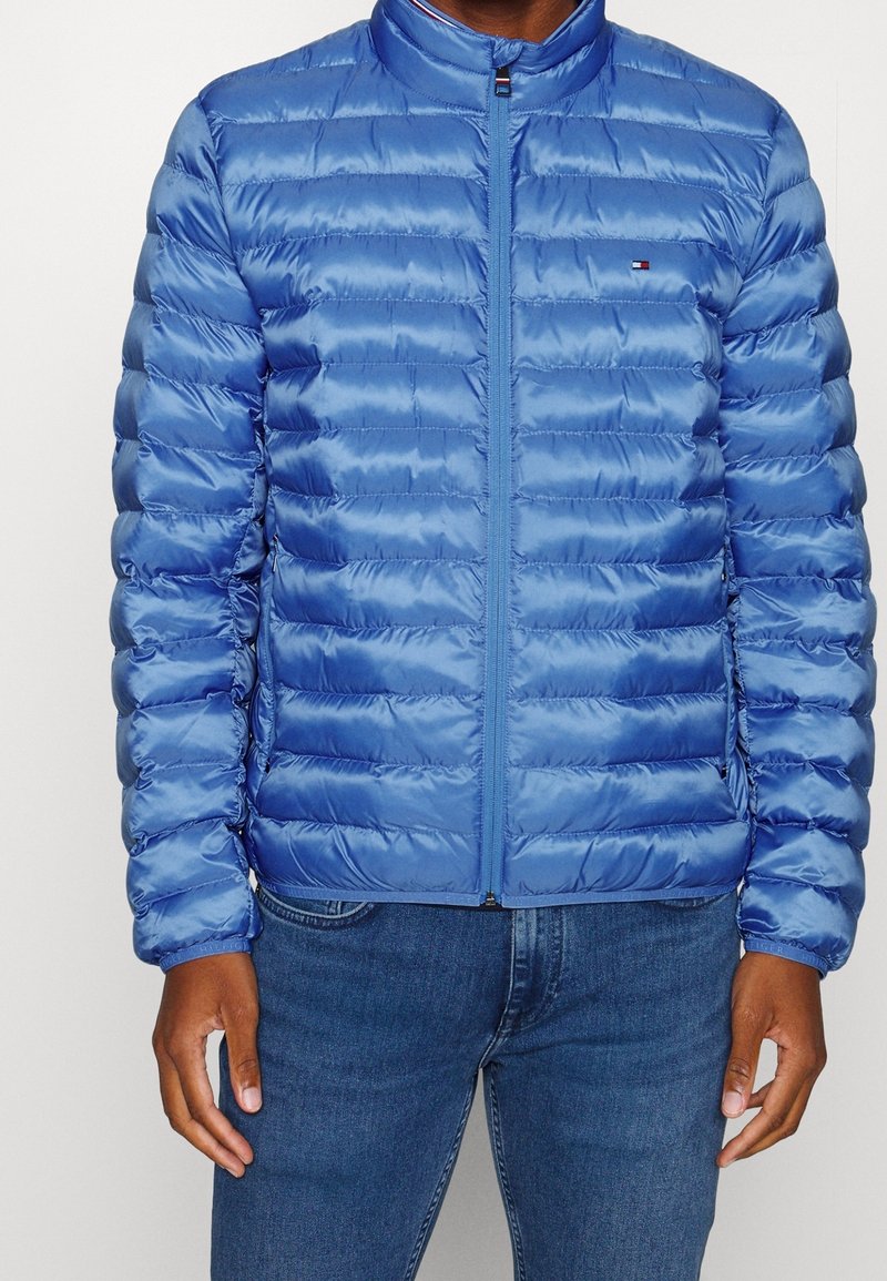 Gepolsterte blaue Jacke mit hohem Kragen und Frontreißverschluss, mit glänzender Textur und horizontalem Steppmuster.