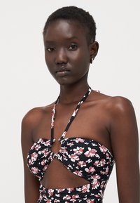 Black floral bikini top featuring small pink and white flowers, cut-out design, halter straps, and a ring detail at the center.