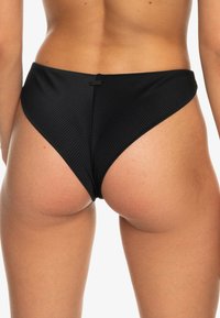 Čierne bikiny s vysokým pásom a rebrovanou textúrou, zakriveným strihom a diskrétnym logom značky na zadnej strane. Vhodné na plážové oblečenie.