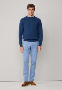 Námornícky sveter s okrúhlym výstrihom a rebrovanými manžetami a lemom, skombinovaný so svetlomodrými chinos nohavicami a hnedými semišovými topánkami. Jednoduchý, ležérny dizajn, minimálne detaily.