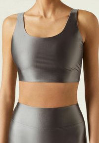 Gray sports bra with a smooth, satin-like texture, featuring a scoop neck and wide straps, paired with a matching high-waisted bottom.