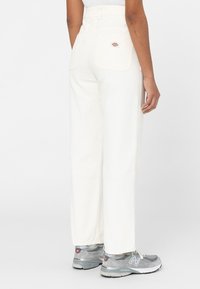 Witte high-waisted broek met een rechte pijp, gemaakt van denim. Heeft twee achterzakken en een logopatch. Draagt met grijze sneakers.