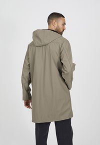 Giacca impermeabile beige con cappuccio, caratterizzata da maniche lunghe e taglio dritto. Tessuto liscio e impermeabile senza motivi visibili.