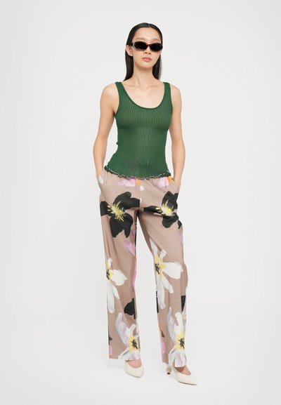 Top verde a costine con orlo scallop abbinato a pantaloni beige con stampa floreale caratterizzata da fiori neri e rosa. Modella con occhiali da sole.