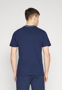 Námořnická modrá bavlněná tričko s krátkým rukávem a kulatým výstřihem, obklopené bílým lemem kolem límce. Jednoduchý design, bez viditelných vzorů.