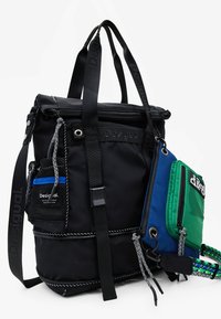Black nylon backpack with multiple straps, zippered compartments, and a detachable colorful pouch featuring green, blue, and black accents.