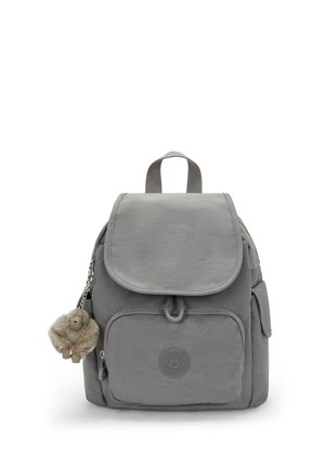 Petit sac à dos gris avec une poche zippée à l'avant, une fermeture à rabat, des poches latérales, une poignée supérieure et un porte-clés en peluche de singe pendu sur le côté gauche.