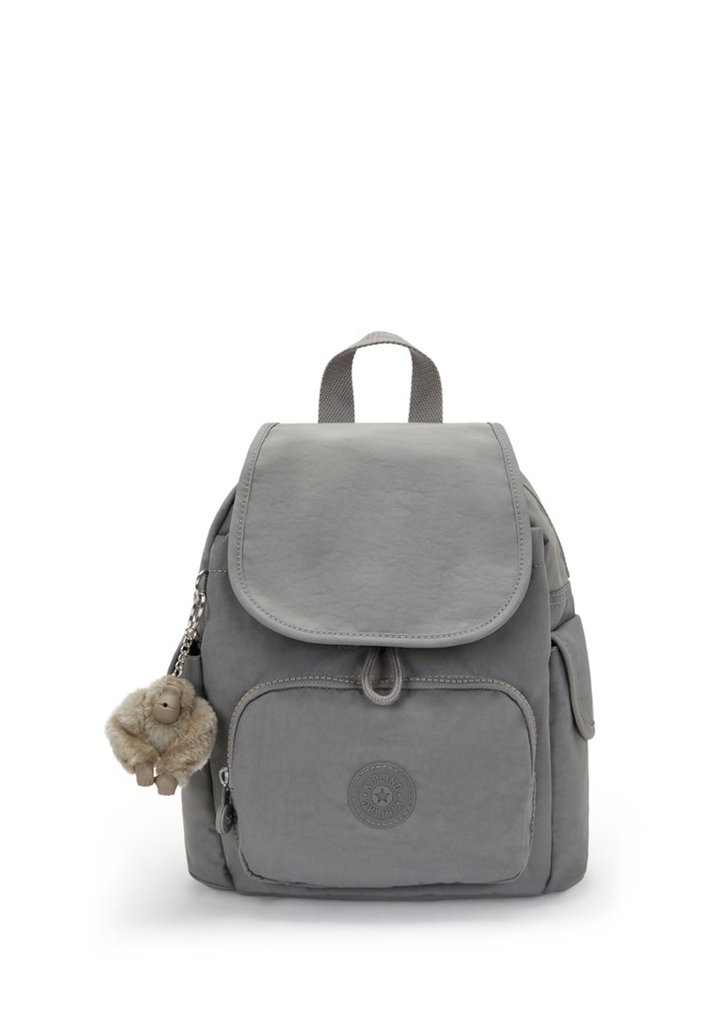 Petit sac à dos gris avec une poche zippée à l'avant, une fermeture à rabat, des poches latérales, une poignée supérieure et un porte-clés en peluche de singe pendu sur le côté gauche.