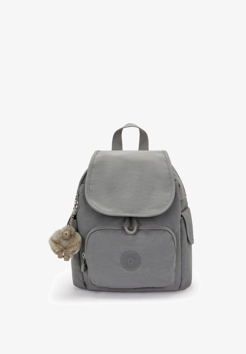 Petit sac à dos gris avec une poche zippée à l'avant, une fermeture à rabat, des poches latérales, une poignée supérieure et un porte-clés en peluche de singe pendu sur le côté gauche.