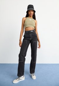 Top corto oliva, pantalones vaqueros de pierna ancha negros con costuras en contraste y zapatillas grises. Los accesorios incluyen un sombrero de cubo negro. Un look simple y casual.