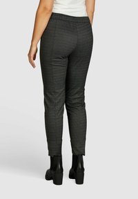 Pantalons fuselés à motif noir avec un tissu texturé, dotés d'une taille élastique et de fentes au niveau des chevilles, associés à des bottes noires chunky.