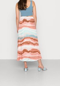 Maxihame dengan pola bergelombang dalam warna coral, merah muda, dan biru muda. Dipadukan dengan crop top biru berpola rib yang cocok dan sepatu mule bertumit blok biru muda.