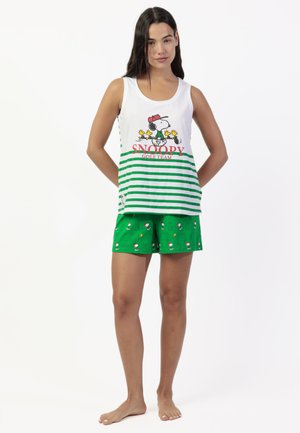 Mujer de pie descalza con camiseta blanca sin mangas con Snoopy y rayas verdes, combinada con pantalones cortos verdes con pequeños dibujos de Snoopy.