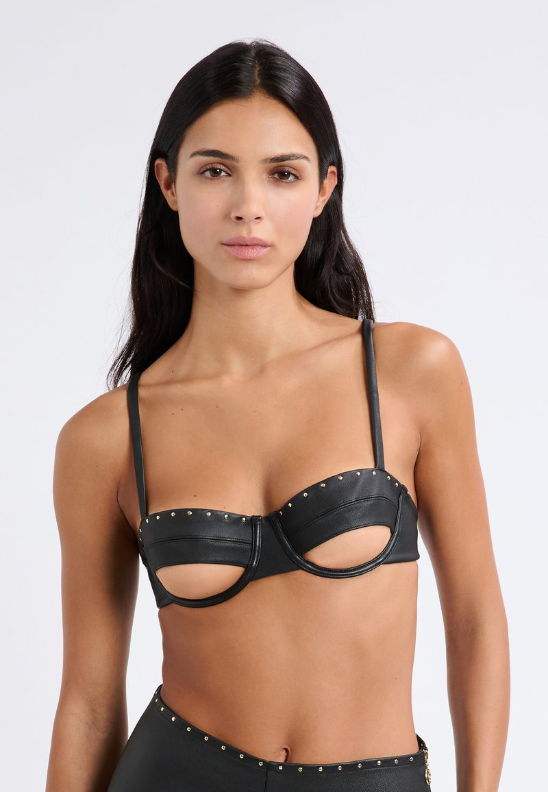 Reggiseno in pelle nera con design a ritaglio, borchie dorate lungo il bordo superiore e spalline sottili e regolabili. Texture liscia con coppe strutturate.