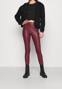 Burgundiska imitationläderleggings, figursydd design, hög midja, kombinerade med en svart kort ribbad topp och en svart denimjacka, samt kraftiga snörskor.