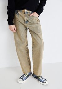 Light blue denim jeans with a relaxed fit, visible pockets, and a faded texture, paired with dark, patterned sneakers.