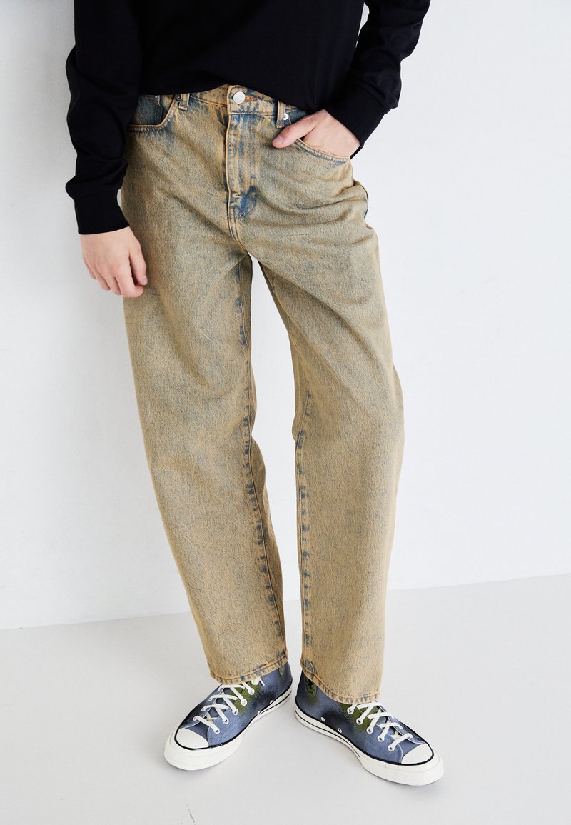 Light blue denim jeans with a relaxed fit, visible pockets, and a faded texture, paired with dark, patterned sneakers.