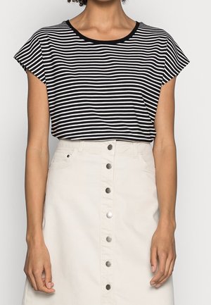Woman wearing a black and white striped short-sleeve top tucked into a high-waisted white skirt with front buttons.