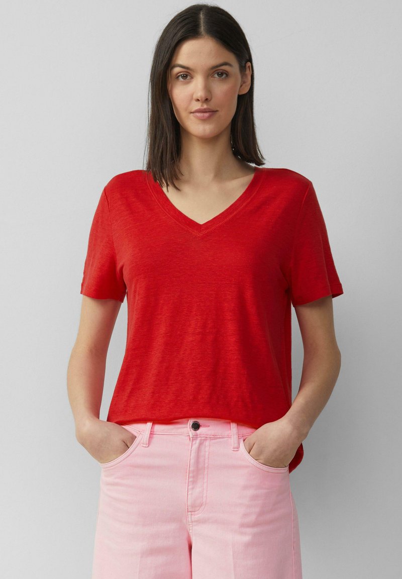 Rode V-hals t-shirt met korte mouwen, gemaakt van lichtgewicht stof, gecombineerd met roze jeans. Het t-shirt heeft een ontspannen pasvorm en een subtiele textuur.