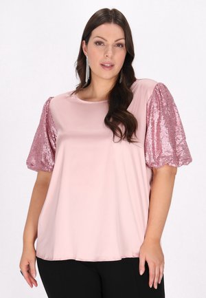 Lys pink bluse med korte, puffede, pailletbesatte ærmer, glat tekstur, rund udskæring og løs pasform. Sorte bukser synlige forneden.