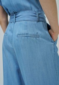 Pantalones de mezclilla anchos de color azul claro con una cintura alta, que presentan una textura suave, bolsillos traseros y un sutil detalle del logo cerca del bolsillo.