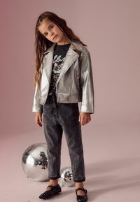Sömsilver metallic läderjacka, svart grafisk t-shirt med leopardtryck, grå denimbyxor och svarta nitar i platta skor.