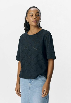 Haut noir à manches courtes avec un motif en vague, présentant un col rond et un tissu texturé. Associé à une jupe en denim bleu clair.