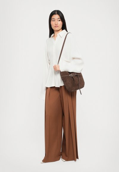 Brown suede shoulder bag with a silver hardware accent, paired with a white button-up shirt and brown wide-leg pants.