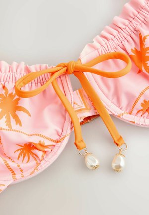 Różowy top bikini z pomarańczowym nadrukiem palm, pomarańczową kokardą do wiązania na środku i dwoma białymi koralikami przypominającymi perły zwisającymi z końcówek wiązania.
