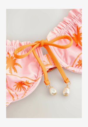 Różowy top bikini z pomarańczowym nadrukiem palm, pomarańczową kokardą do wiązania na środku i dwoma białymi koralikami przypominającymi perły zwisającymi z końcówek wiązania.