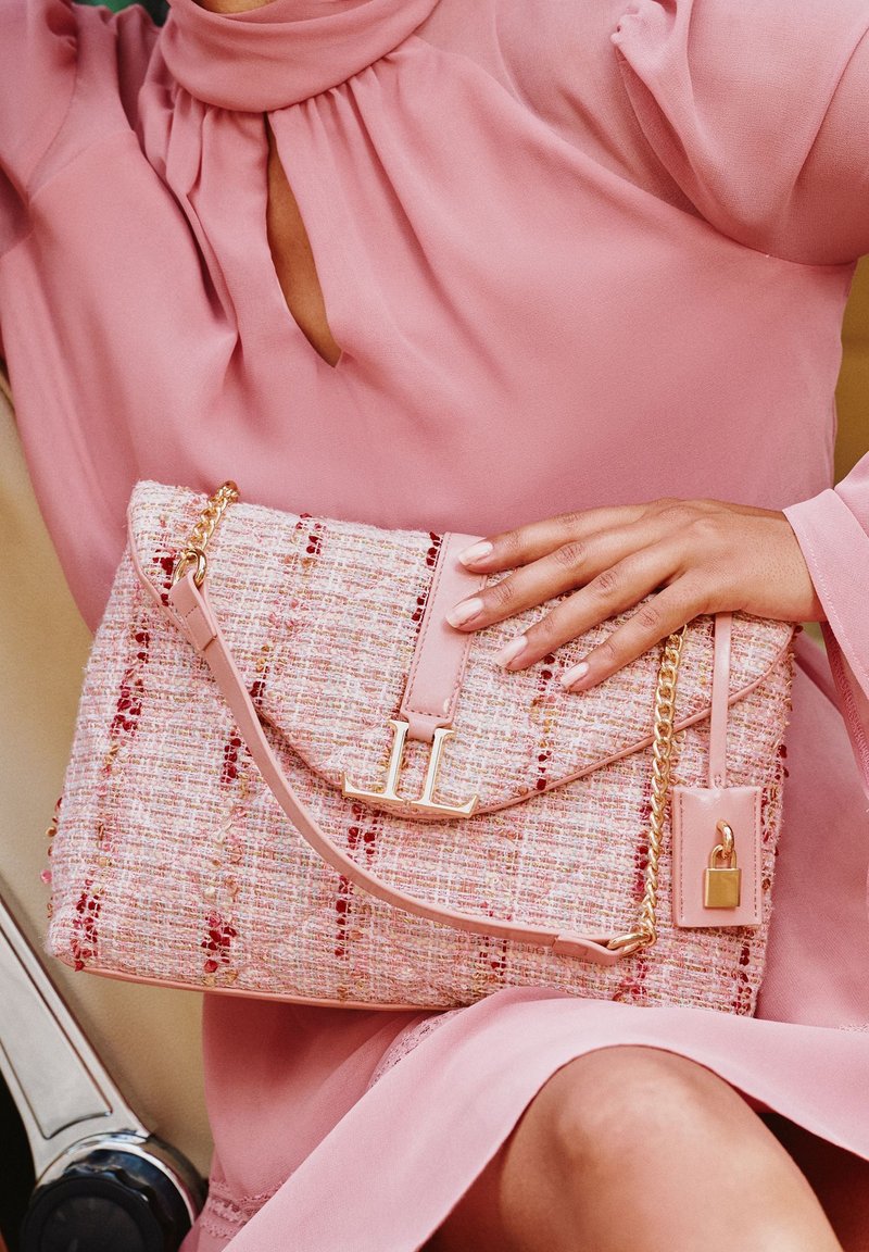 Borsa in tweed rosa con hardware dorato, chiusura a pattina e tracolla a catena. Caratteristiche notevoli includono un logo "LL" e texture accentuate.