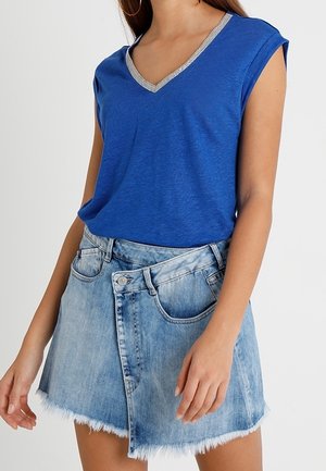 Blå V-hals t-shirt med sølvkant, parret med en lyseblå jeansnederdel med en frayed kant og asymmetrisk front.