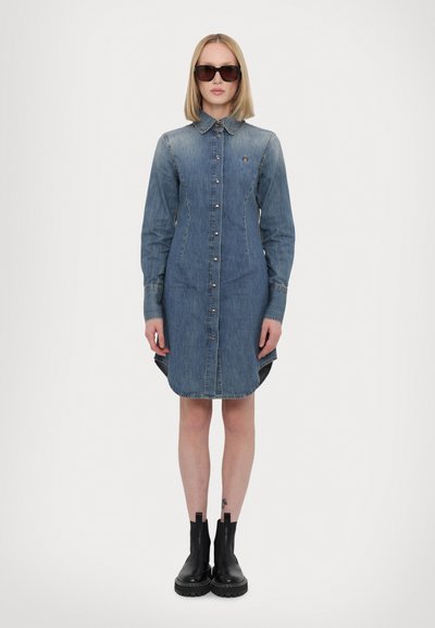 Denim kleita ar pogu priekšpusi, apkakles kaklu un sudraba pogām. Ar garām piedurknēm un augstāk-zemākām malām. Valkāta ar melniem potīšu zābakiem.