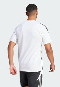 Camiseta blanca de manga corta con rayas laterales negras, material de algodón suave y un ajuste relajado. Sin gráficos ni patrones notables.